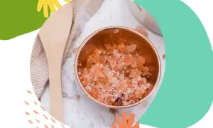 Miedziana miseczka z różowym, domowy peeling do twarzy. Obok drewniana łyżka i ręcznik.