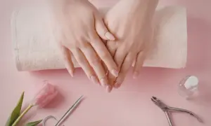 Delikatne dłonie z perfekcyjnym manicurem kombinowanym, obok różowy tulipan, cążki i buteleczka lakieru.