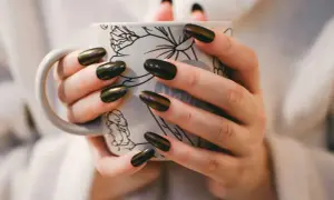 Dłonie z pięknym, błyszczącym japońskim manicure trzymają kubek z delikatnym wzorem.