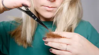 Kobieta z blond włosami przycina końcówki nożyczkami, ucząc się, jak samemu obciąć włosy z tyłu.
