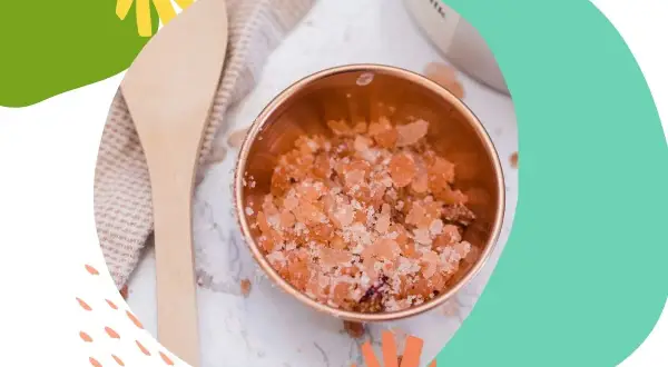 Miedziana miseczka z różowym, domowy peeling do twarzy. Obok drewniana łyżka i ręcznik.