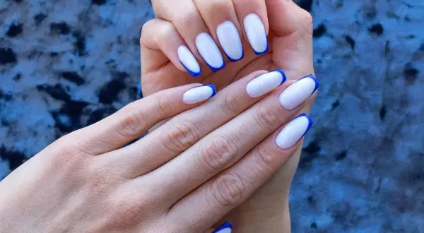 Dłonie z paznokciami w stylu niebieski french. Klasyczny manicure z odważnym, kobaltowym akcentem.