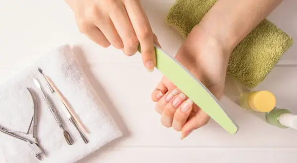 Dłonie z naturalnymi paznokciami, pilniczek, cążki i inne akcesoria do manicure. Dowiedz się, jak szybko zapuścić paznokcie.