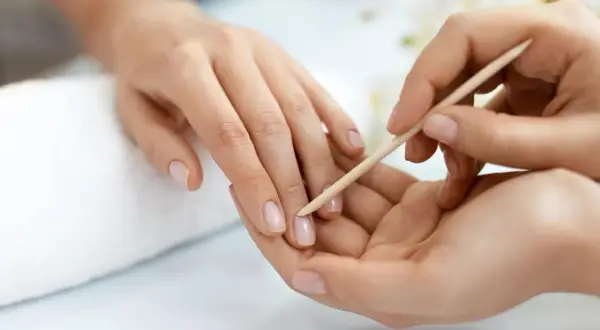 Delikatne dłonie poddawane są zabiegowi manicure biologicznego. Drewniany patyczek delikatnie odsuwa skórki, przygotowując paznokcie do dalszej pielęgnacji.