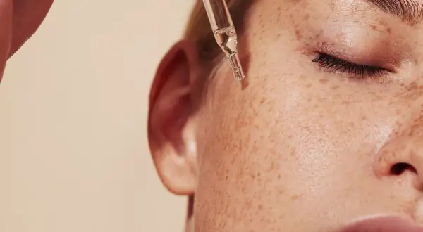 Kropla serum z pipety spada na piegowatą skórę. Czy to retinol? Co to jest retinol i jak działa na skórę?