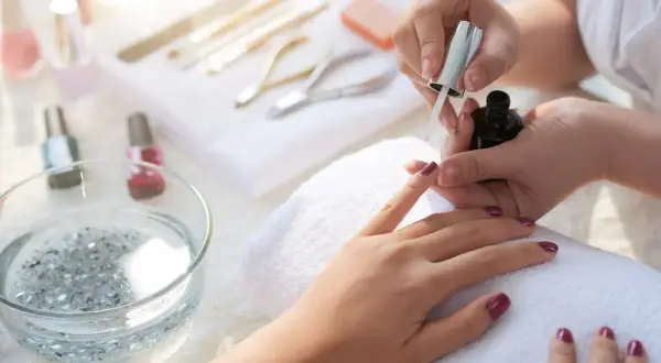 Aplikacja top coat na paznokcie. To ostatni etap manicure, który utrwala lakier i nadaje połysk.