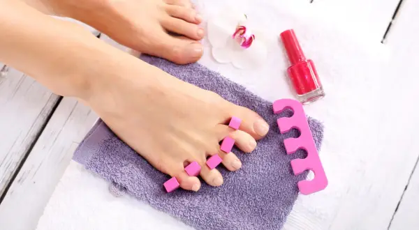 Przygotowanie do różowego pedicure hybrydowego: stopy na ręcznikach, separatory do palców i lakier.