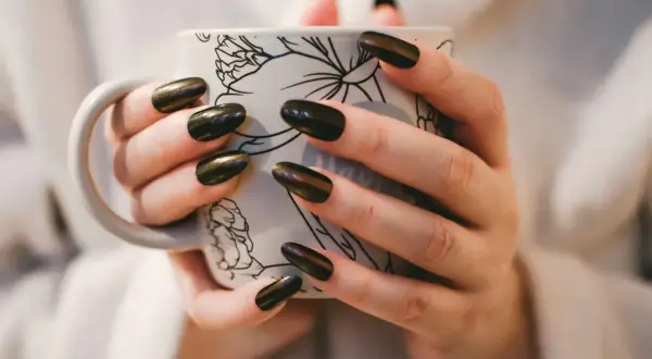 Dłonie z pięknym, błyszczącym japońskim manicure trzymają kubek z delikatnym wzorem.