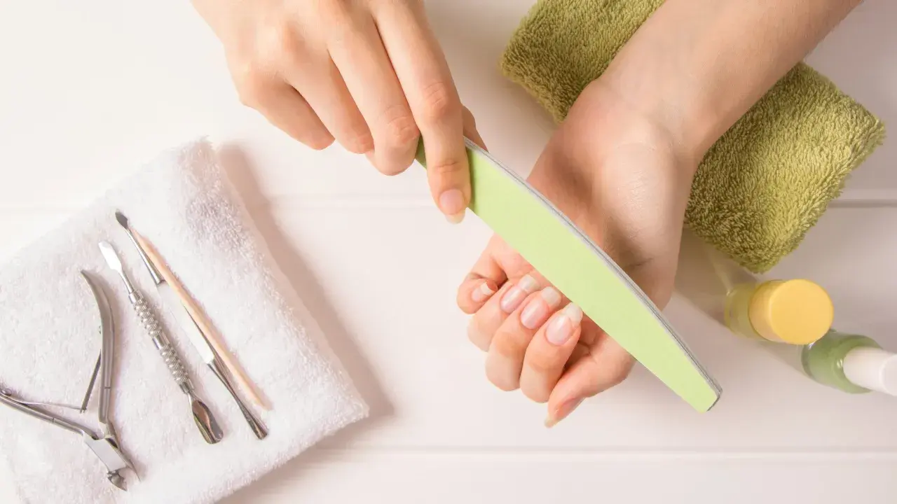 Dłonie z naturalnymi paznokciami, pilniczek, cążki i inne akcesoria do manicure. Dowiedz się, jak szybko zapuścić paznokcie.