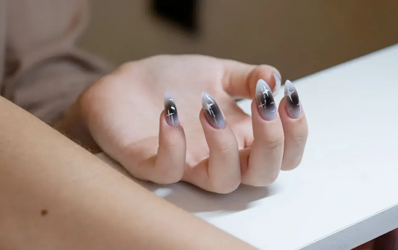 Dłoń z paznokciami w stylu aura nails, zdobionymi gradientem czerni i bieli oraz błyszczącymi gwiazdkami.