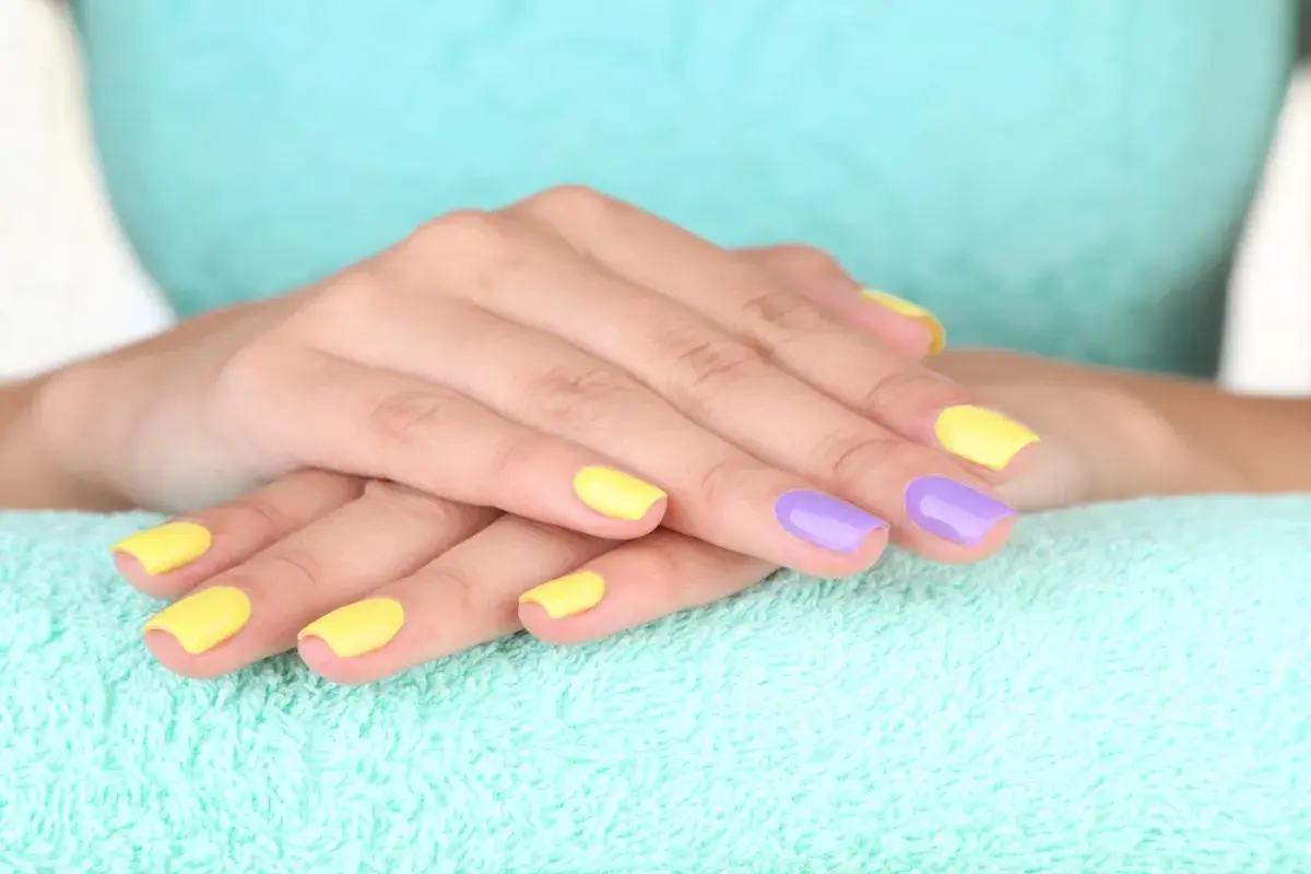 Dłonie z paznokciami pomalowanymi na żółto i fioletowo. To przykład, jak może wyglądać manicure klasyczny co to za styl.