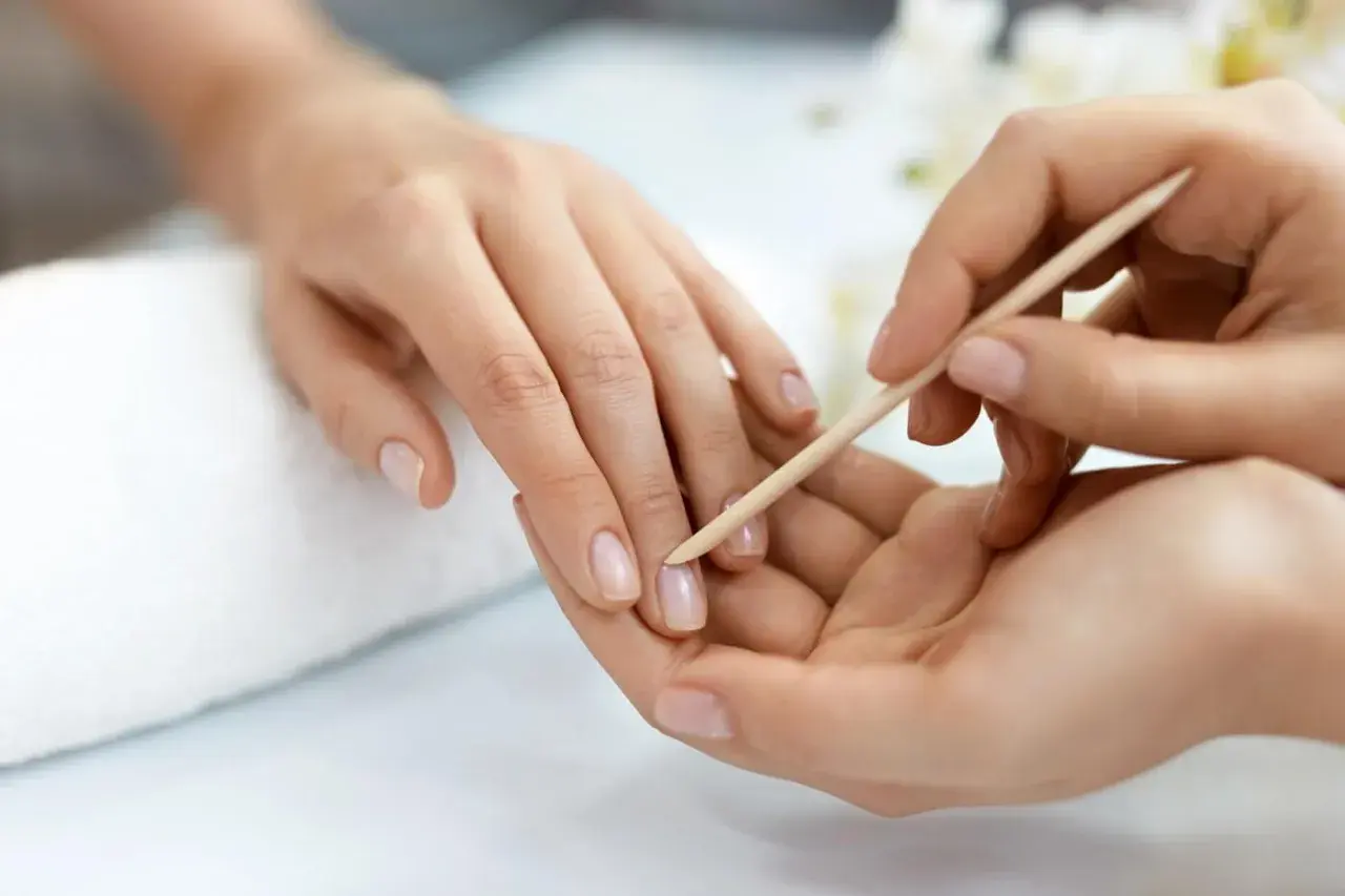 Delikatne dłonie poddawane są zabiegowi manicure biologicznego. Drewniany patyczek delikatnie odsuwa skórki, przygotowując paznokcie do dalszej pielęgnacji.