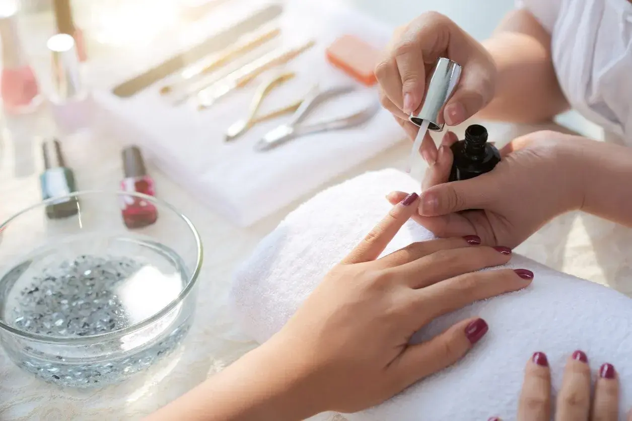 Aplikacja top coat na paznokcie. To ostatni etap manicure, który utrwala lakier i nadaje połysk.
