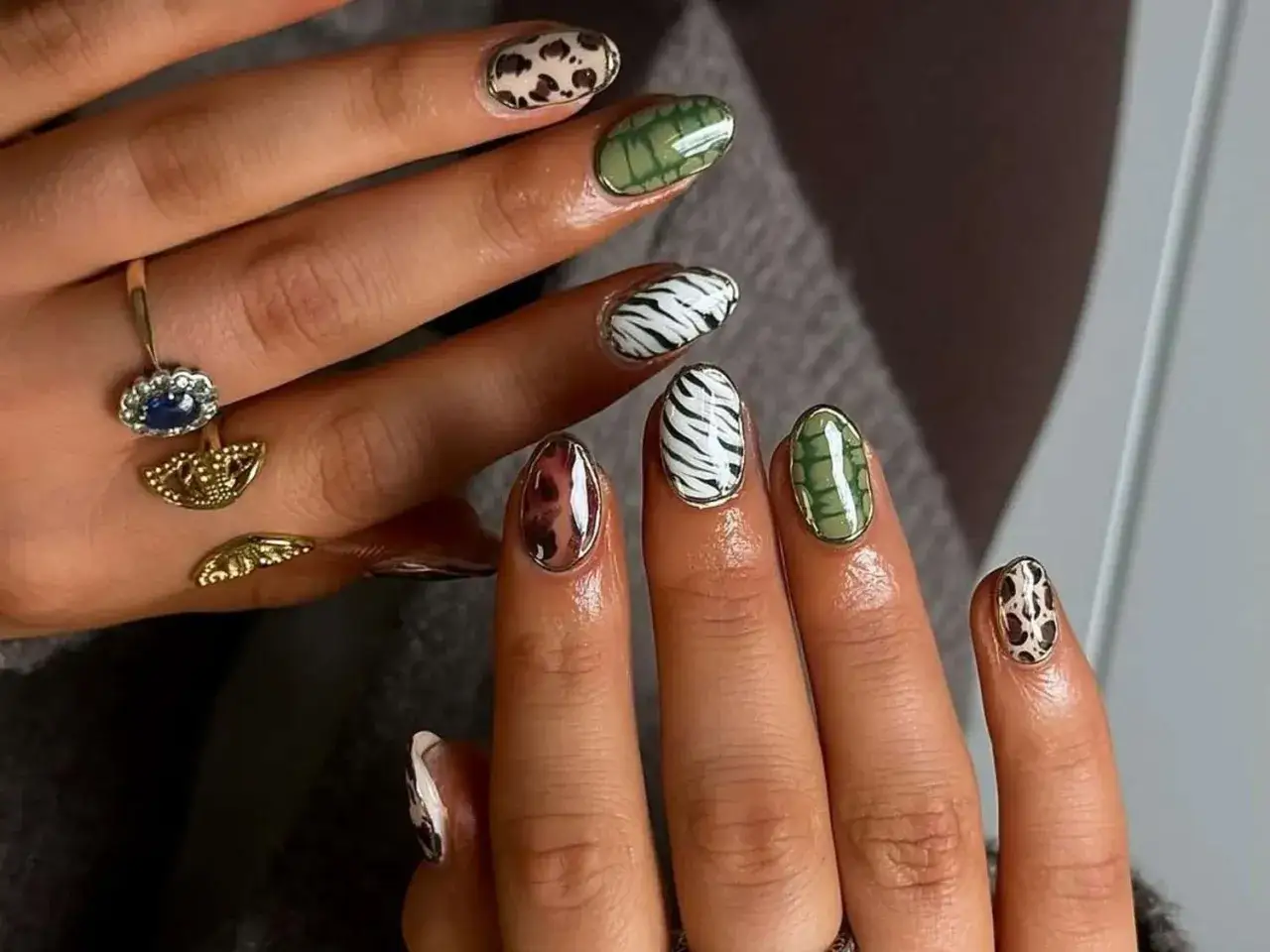 Dłonie z bardzo krótkimi paznokciami w zwierzęce wzory: pantera, zebra, krokodyl. Złota biżuteria dodaje elegancji.