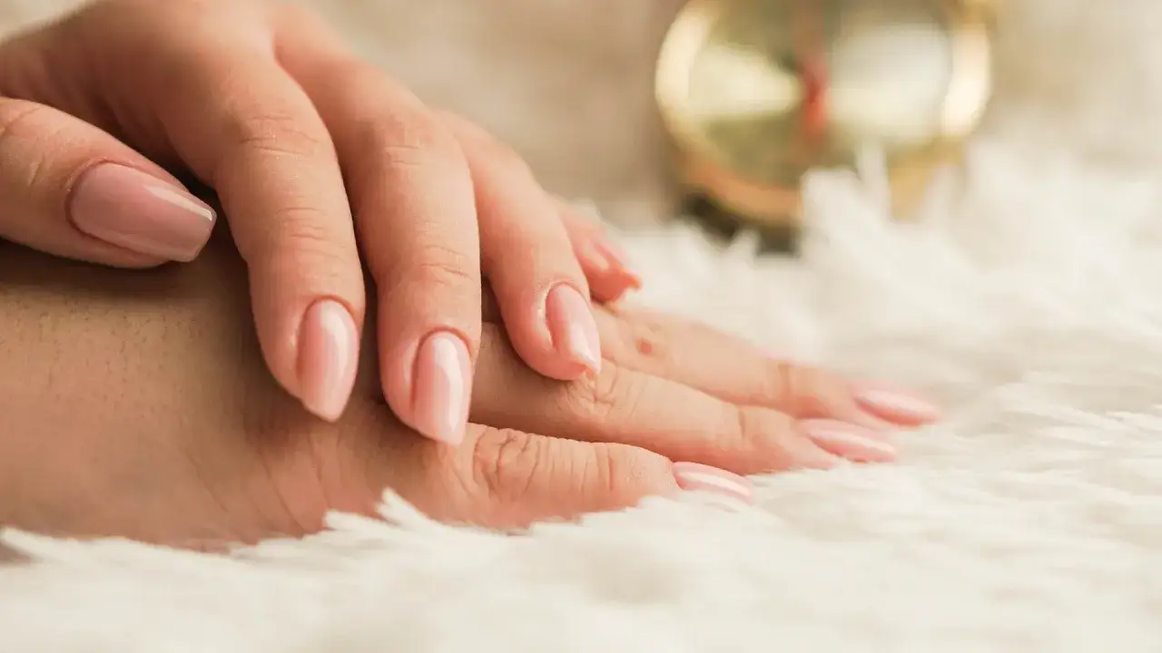 Delikatne dłonie z różowym, naturalnym manicure biologicznym na puszystym tle.