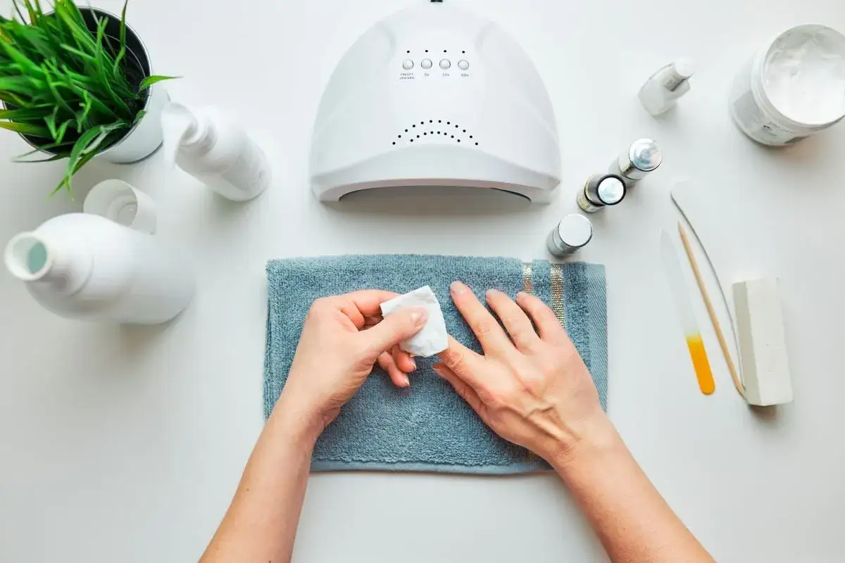 Przygotowanie do manicure hybrydowego: dłonie, lampa UV, lakiery i akcesoria do paznokci.