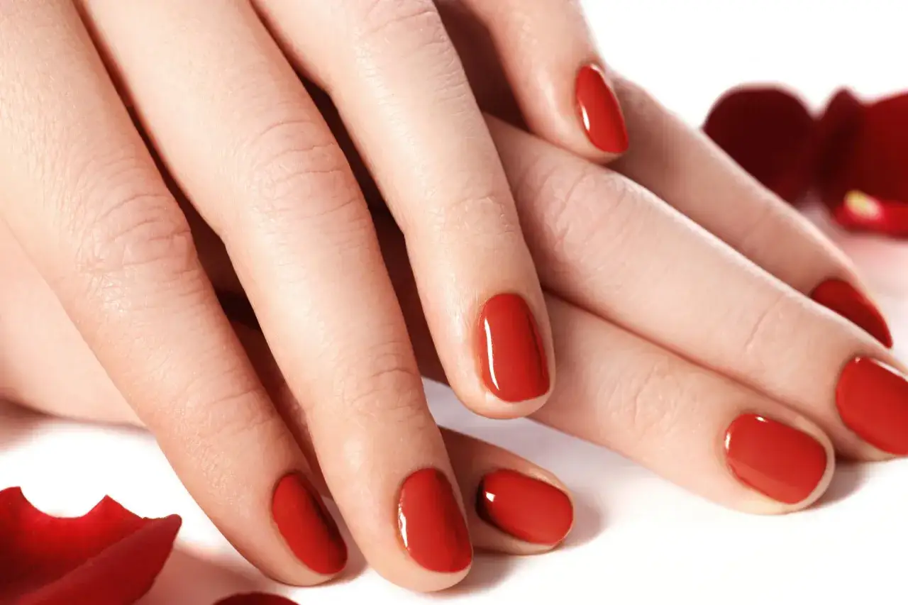 Dłonie z idealnym, czerwonym manicure, niczym tytanowe paznokcie, otoczone płatkami róż.