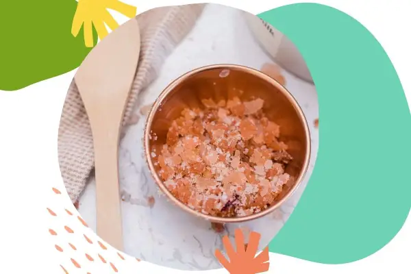 Miedziana miseczka z różowym, domowy peeling do twarzy. Obok drewniana łyżka i ręcznik.