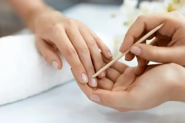 Delikatne dłonie poddawane są zabiegowi manicure biologicznego. Drewniany patyczek delikatnie odsuwa skórki, przygotowując paznokcie do dalszej pielęgnacji.