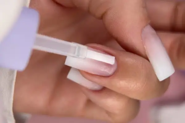 Aplikacja bazy pod hybrydę krok po kroku. Delikatny pędzelek rozprowadza produkt na paznokciu.