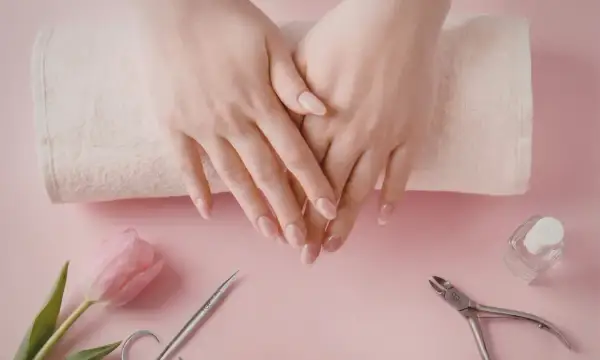 Delikatne dłonie z perfekcyjnym manicurem kombinowanym, obok różowy tulipan, cążki i buteleczka lakieru.
