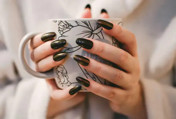 Dłonie z pięknym, błyszczącym japońskim manicure trzymają kubek z delikatnym wzorem.